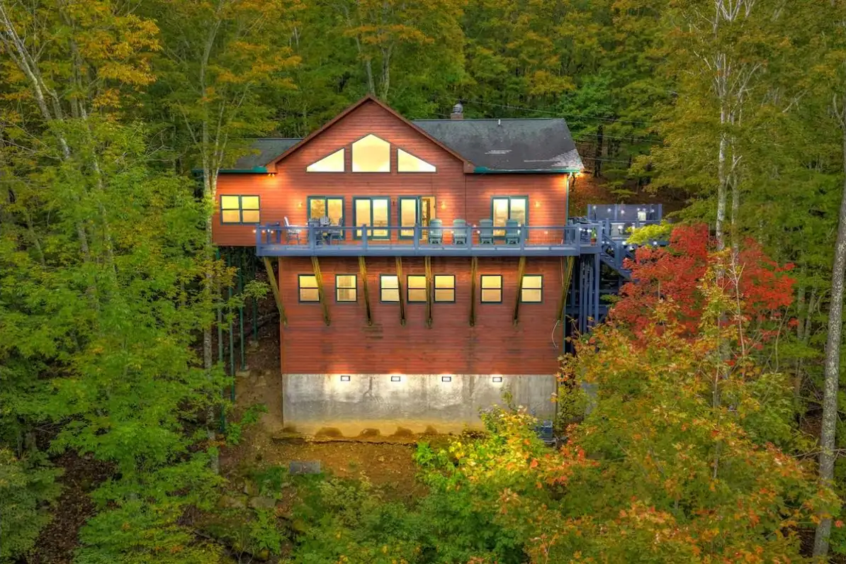 Aerial view of a mountain chalet at dusk showing the full roofline and multi-level decks among autumn trees