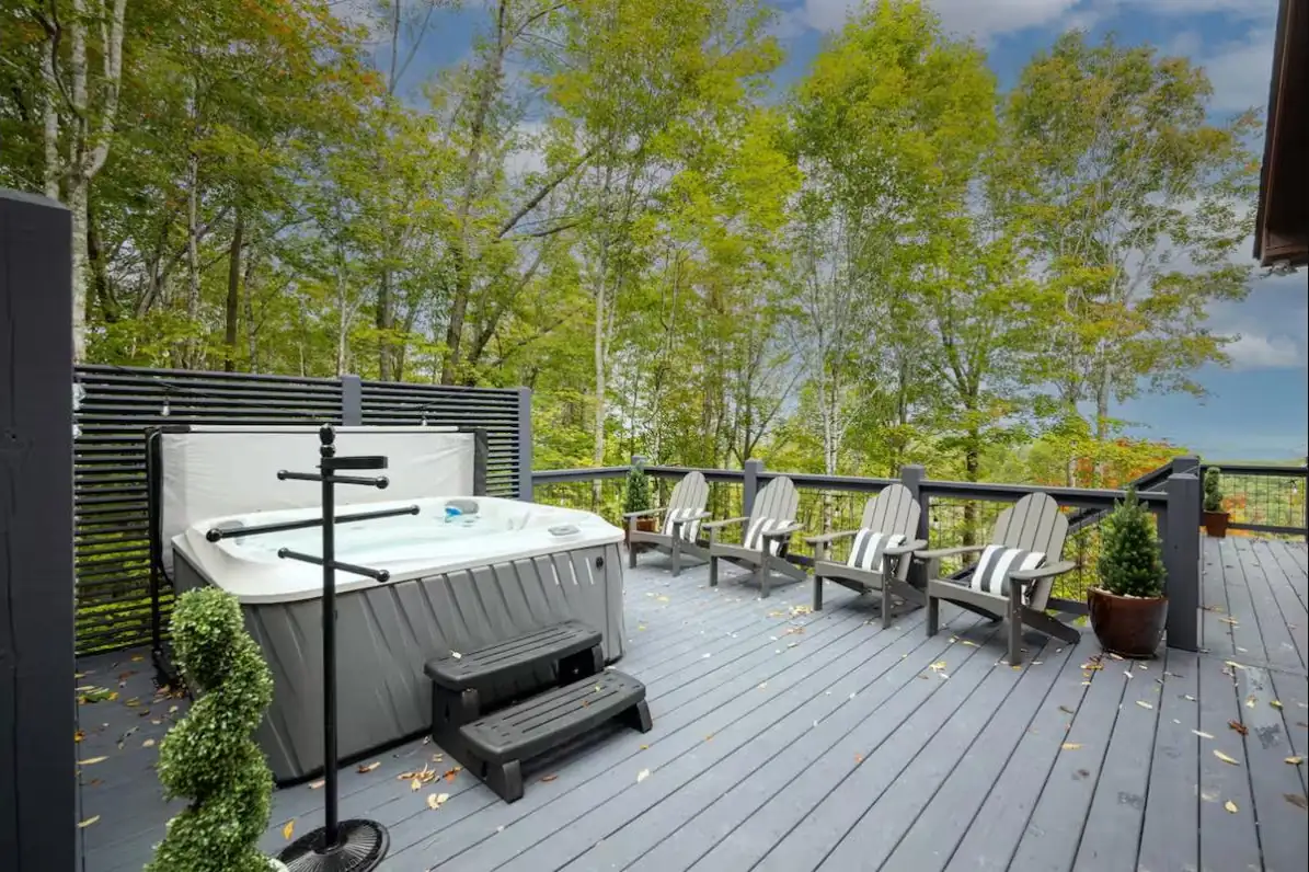 Hot tub on a dark-stained deck with Adirondack chairs and a privacy slat wall