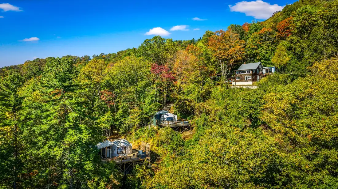 Aerial view of a completed geodesic dome site with deck and hot tub tucked into the forest