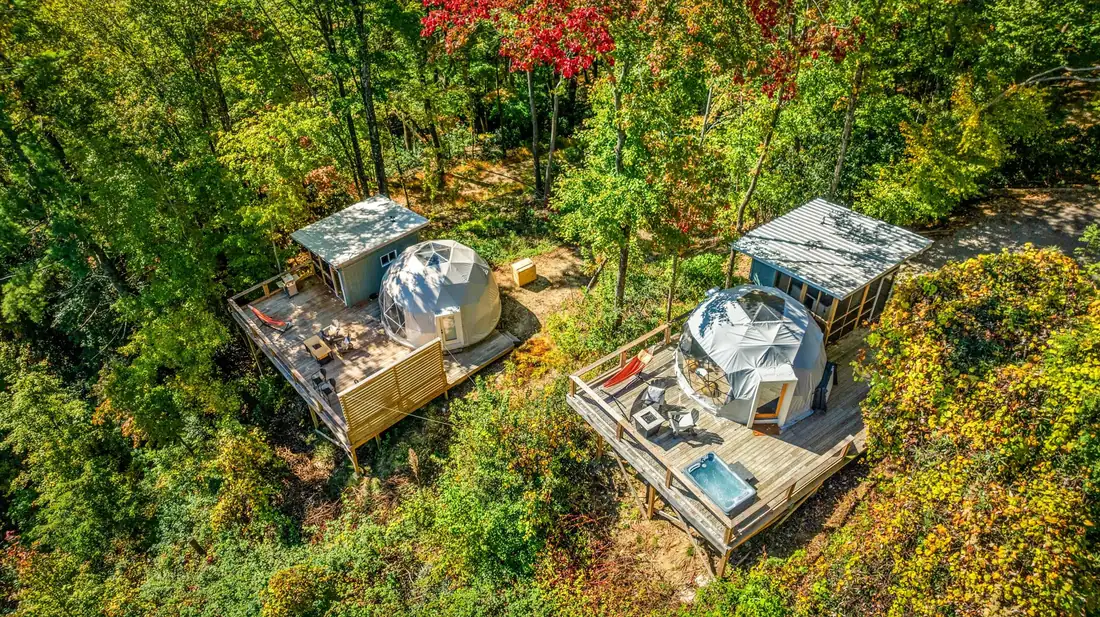Aerial view of two geodesic dome sites with decks and hot tubs in the forest