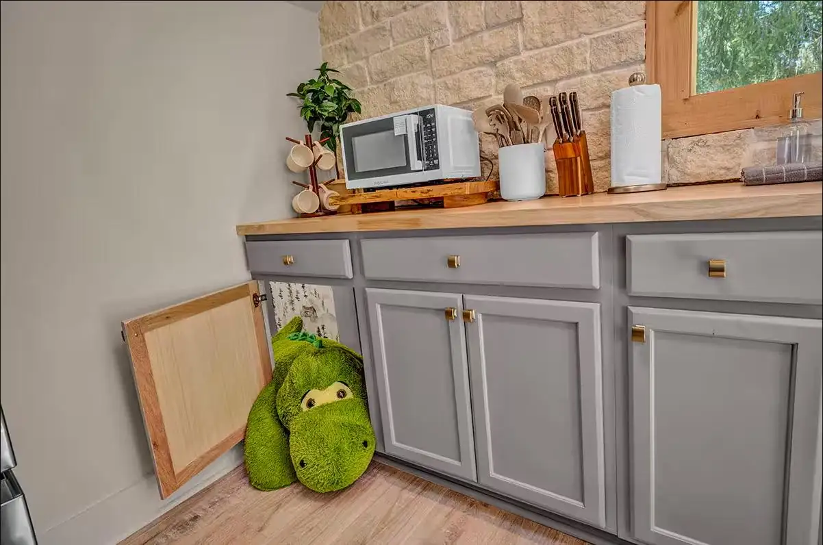 Crawl-through kitchen cabinet passage into a kids play space, with a stuffed dinosaur peeking out