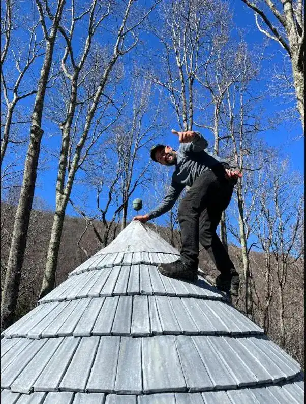 Pro standing on a completed shake roof among winter trees