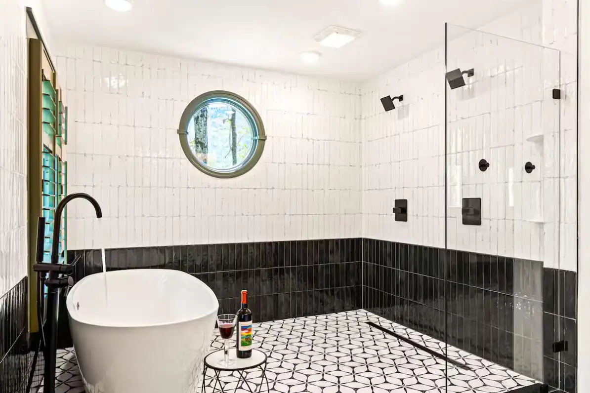 Black-and-white tiled wetroom with freestanding tub, glass shower, and porthole window